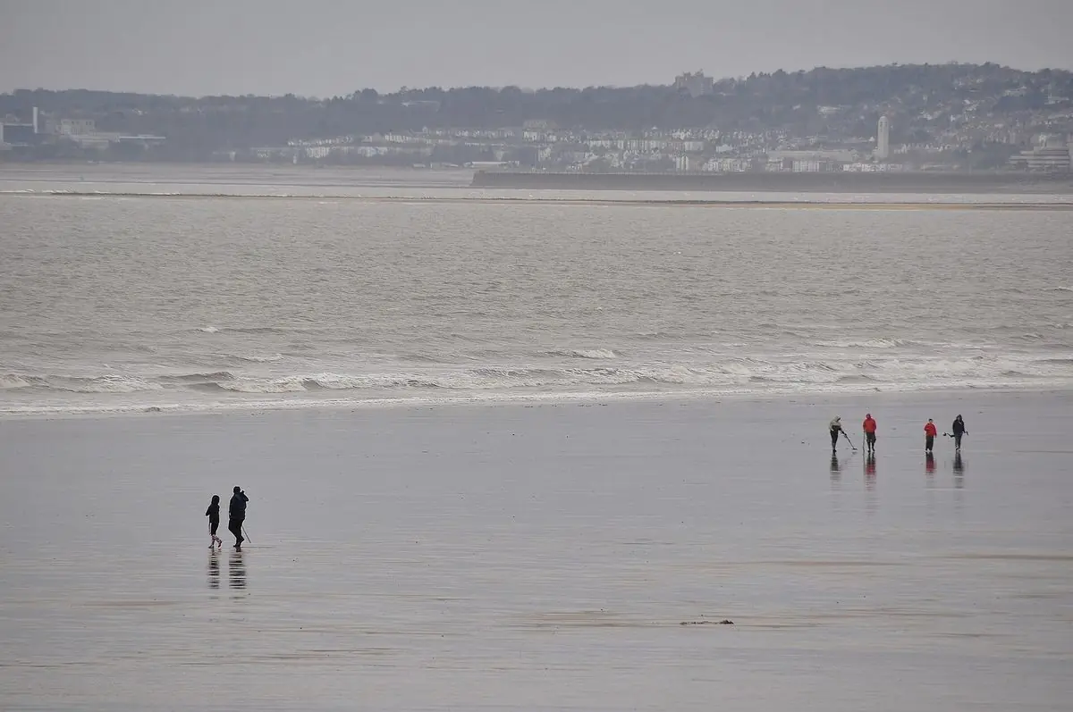 People walking on the wet sand at Aberavon, with the town on the far shore